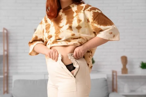 Image of woman trying to do her trousers up after pregnancy weight gain Macclesfield
