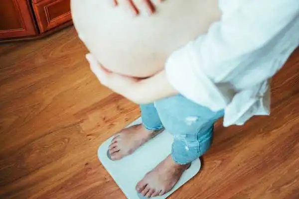 Image of woman weighing herself and experiencing weight gain through pregnancy Macclesfield
